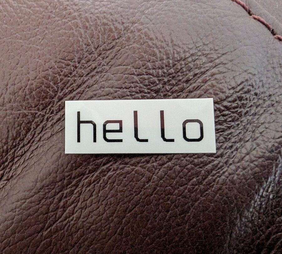 A white label printed with a lowercase 'hello' in black, resting on brown leather
